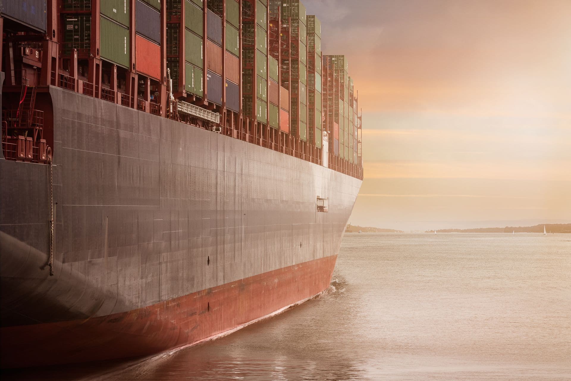 Bow of a cargo ship loaded with containers arriving at sunset